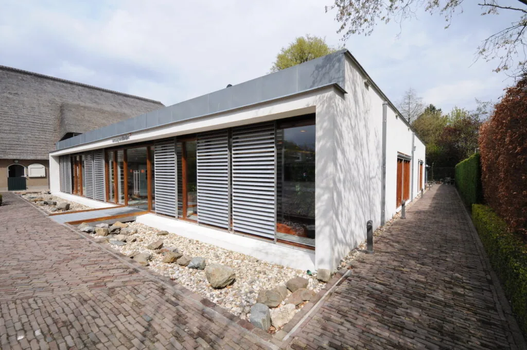 Modern laagbouwgebouw aan de Charloisse Lagedijk met grote ramen en horizontale zonwering, omringd door een bestrate wandelweg en siergrind.